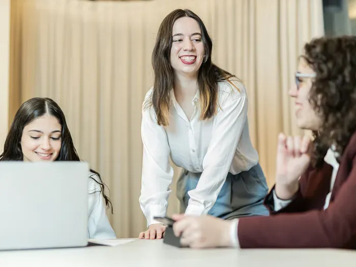 Group of young professionals in formal attire collaborating and smiling during office meeting around table